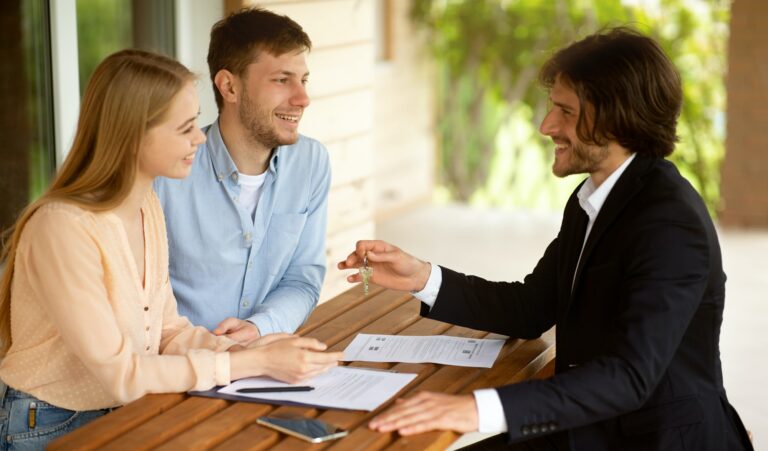 Real estate broker giving house key to millennial couple after signing property agreement at table